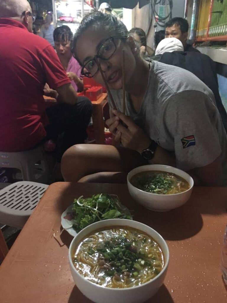 Dee sitting with bowl of noodles in Vietnam.
